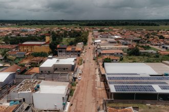 Vista aérea de uma comunidade com painéis solares instalados em telhados, cercada por paisagem verde.